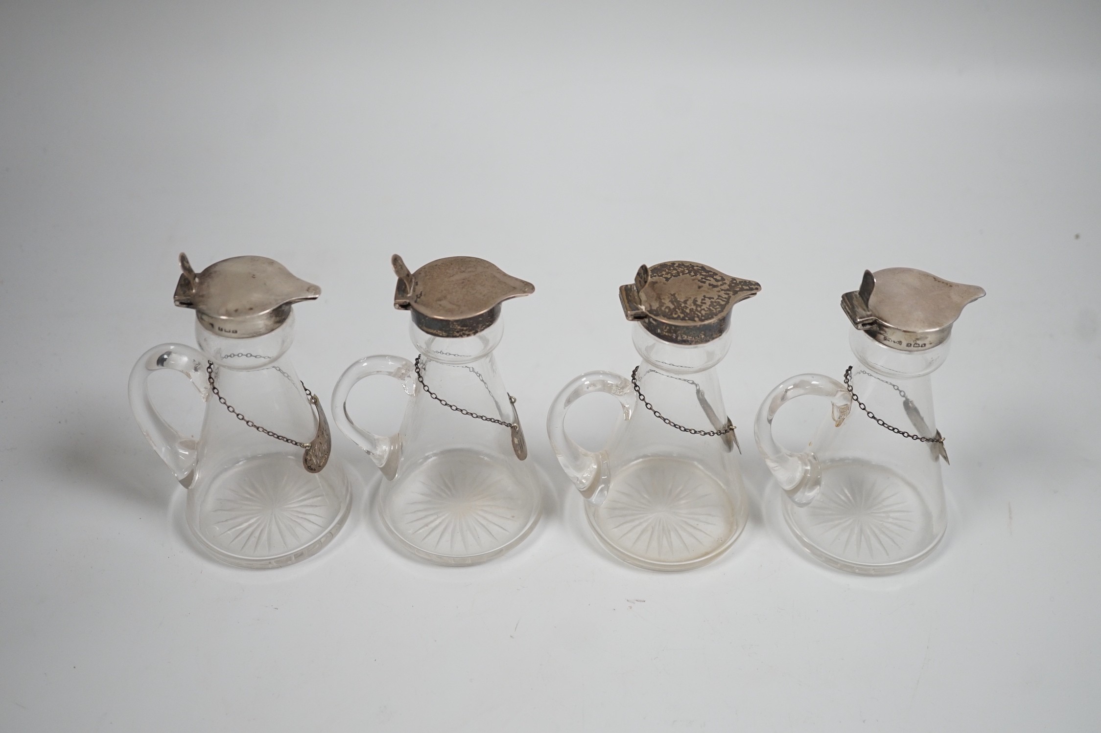 A set of four Edwardian silver mounted glass whisky noggins, H.B. Johnson & Co, Birmingham, 1909, height 12cm, together with a set of four silver whisky labels, same maker, London, 1910.